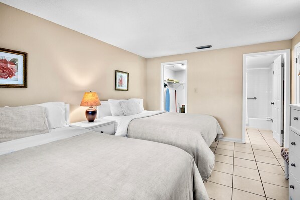 Habitación de hotel con dos camas, una mesita de noche, una lámpara, un cuadro enmarcado y la puerta del baño.