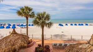 A beach view with palm trees, blue lounge chairs, and thatched umbrellas.