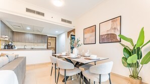 A modern dining area with a central table set for four, surrounded by grey chairs. A large potted plant is on the right.