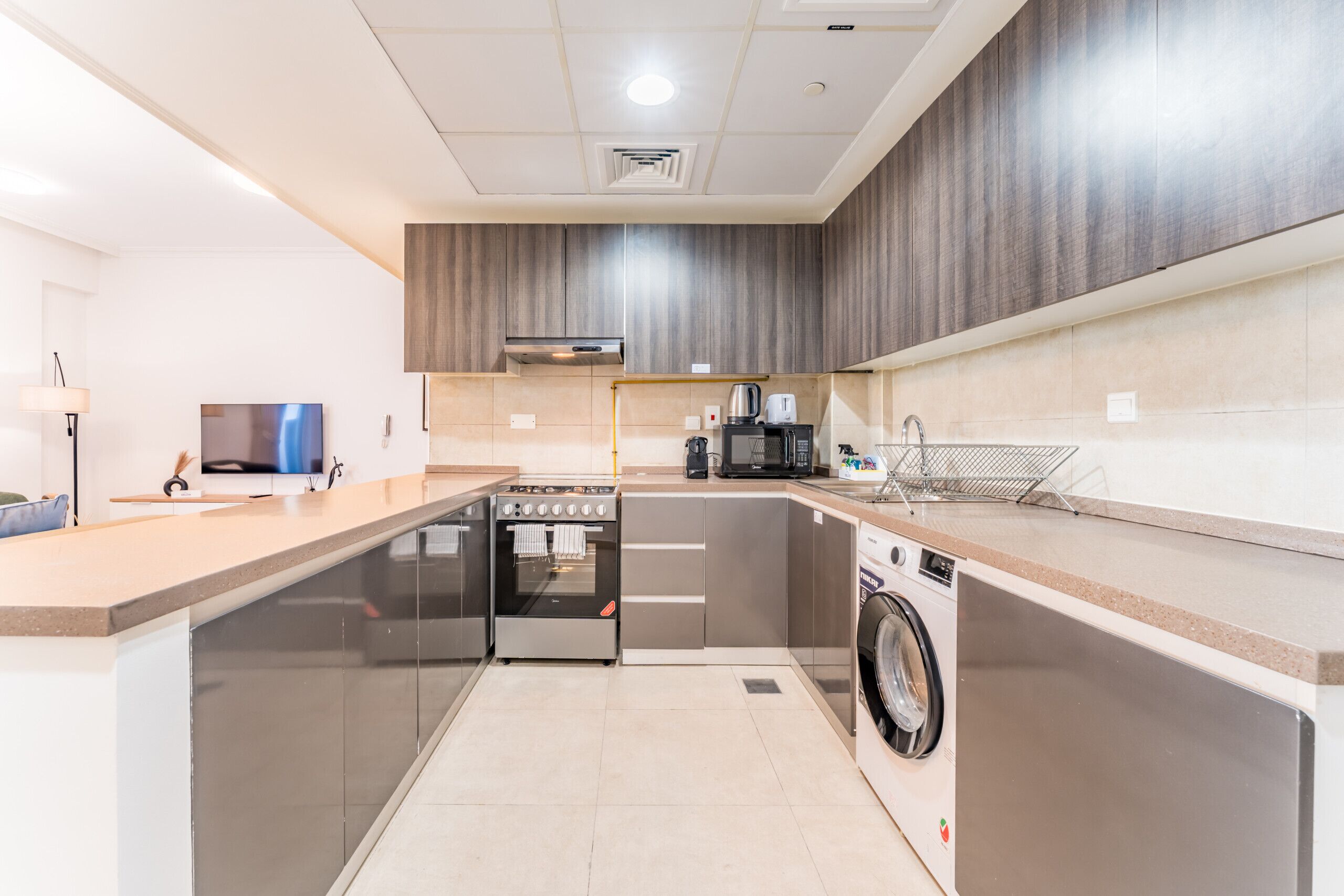 Une cuisine moderne dotée d’un four, d’un micro-ondes et d’un lave-linge intégrés, avec un design épuré et un grand espace de travail.