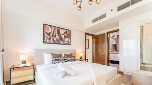 A modern hotel room with a large bed, a bedside table with a lamp, a wall art piece, and a wardrobe.