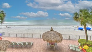 Vista de playa con una sombrilla de paja, sillas de descanso y una valla.
