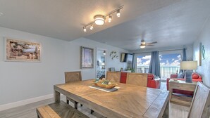 Un comedor con una mesa de madera y bancos, un ventilador de techo y vistas al exterior a través de un ventanal grande.