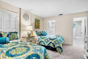 A bedroom with two beds, a nightstand, a lamp, a clock, and a door leading to a bathroom.