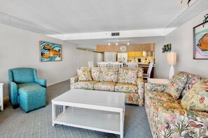 A living room with a sofa, armchair, and coffee table. There is a dining area with a table and chairs.