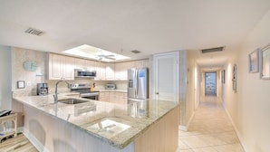 A modern kitchen with a large island, stainless steel appliances, and a clock on the wall.