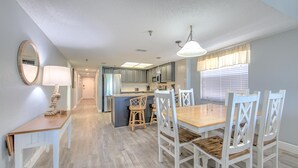 Una cocina moderna con una isla central, muebles blancos y un comedor con mesa de madera y sillas blancas.