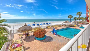 A poolside area with a view of the beach, lounge chairs, and a thatched umbrella.
