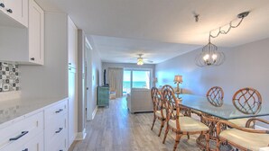 A modern kitchen with white cabinets, a dining area with a glass table and wicker chairs, and a ceiling fan.