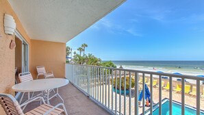 A balcony with a view of the beach, a pool, and outdoor seating.