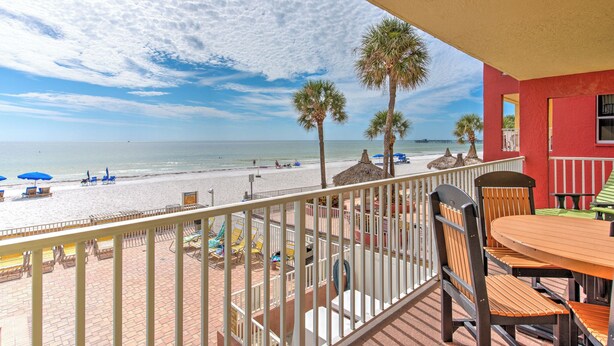 Ein Balkon mit Blick auf den Strand, Palmen und ein rotes Gebäude.