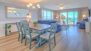 A spacious living room with a wooden dining table, blue chairs, a blue sofa, and a chandelier.