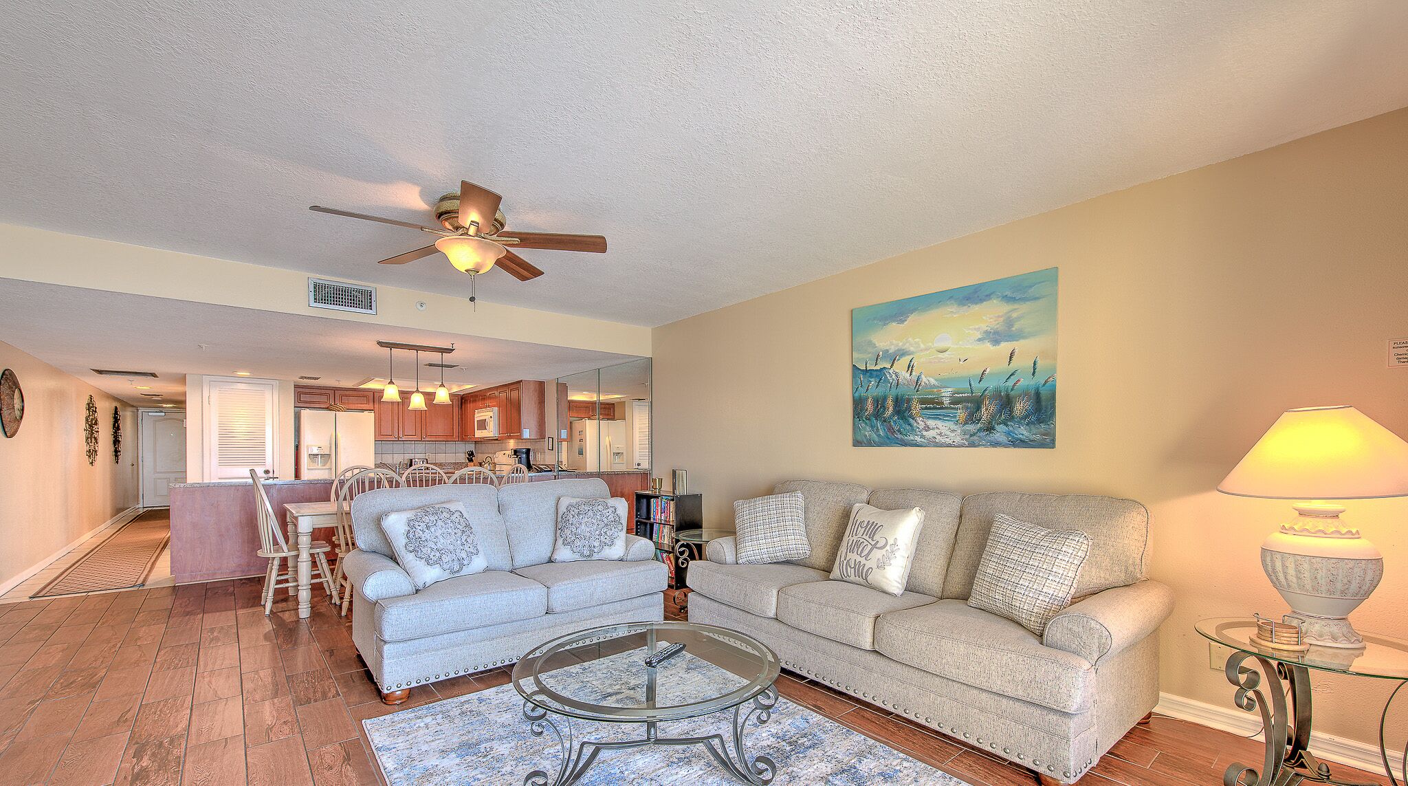 A spacious living room with a sofa set, a coffee table, and a dining area with chairs and a kitchen in the background.