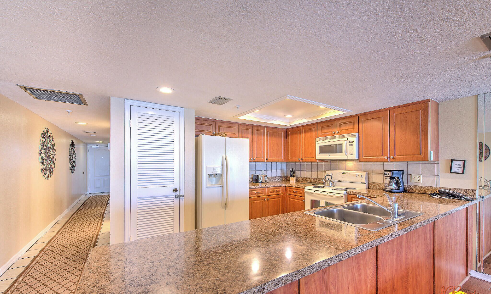Una cocina moderna con encimeras de granito, armarios de madera, pileta de acero inoxidable y microondas integrado.