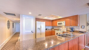 Una cocina moderna con encimeras de granito, armarios de madera, pileta de acero inoxidable y microondas integrado.