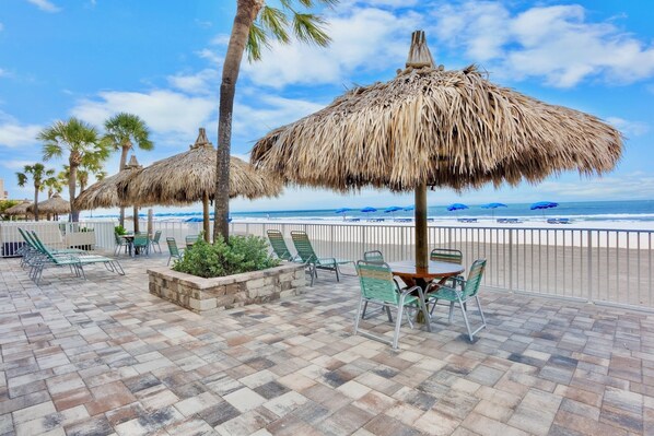 A beachside patio with thatched umbrellas, lounge chairs, and a table with chairs.