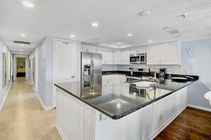 A modern kitchen with white cabinetry, stainless steel appliances, and a large island with a sink.