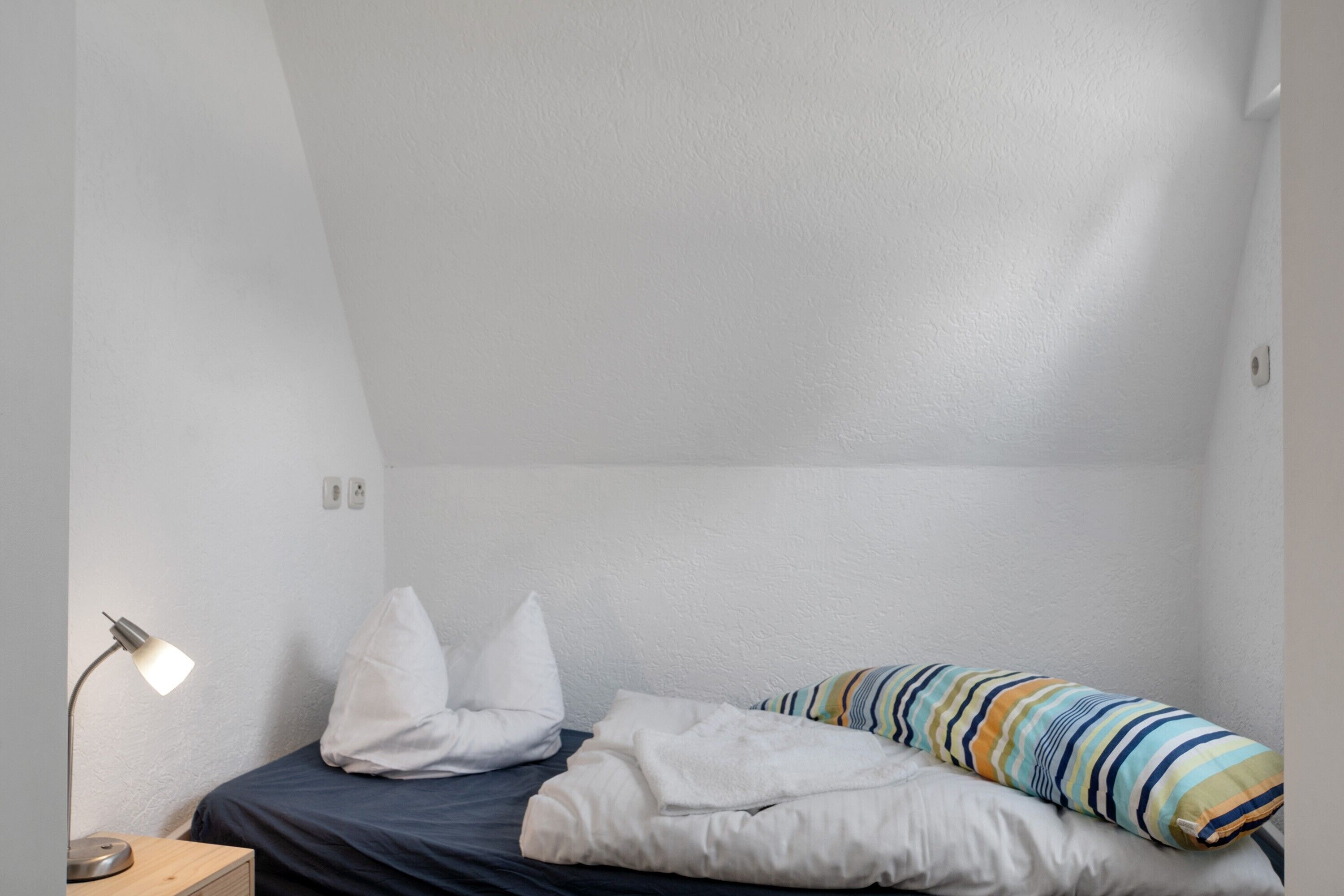 Una habitación pequeña con una cama individual, un escritorio, una lámpara y un almohadón a rayas.