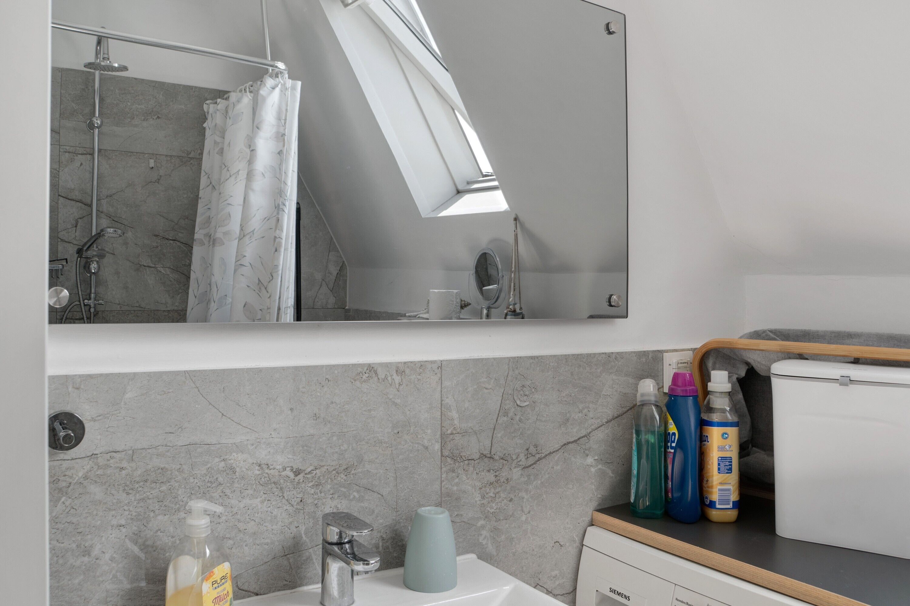 Une salle de bain moderne équipée d’une douche, d’un lavabo, d’un miroir et de produits de toilette disposés sur le comptoir.