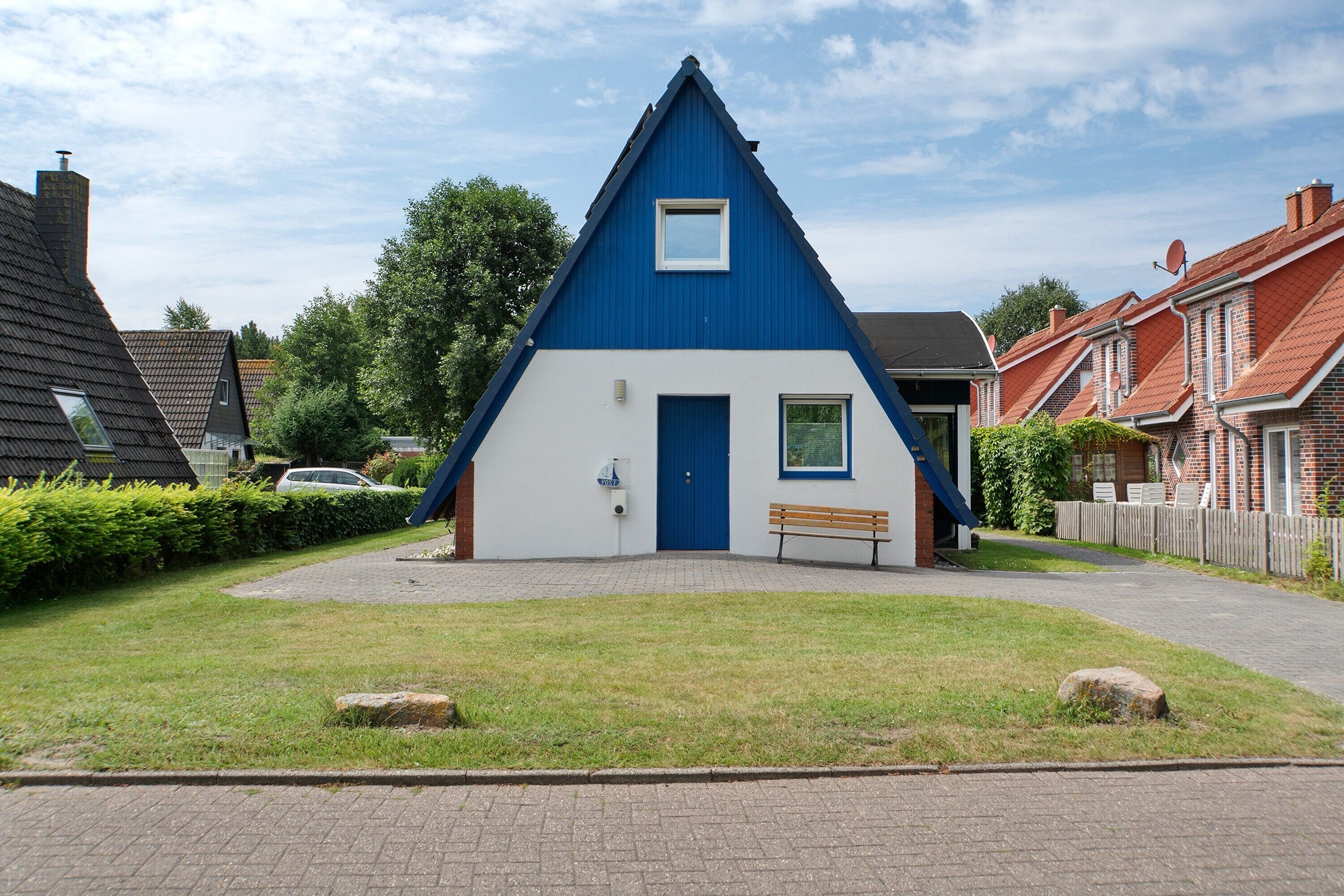 Un bâtiment bleu et blanc avec une porte et une fenêtre, entouré de pelouse et bordé d’un chemin pavé.
