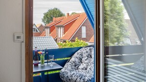 Een kamer met uitzicht op omliggende huizen, een tafel met fles en glas, en een fauteuil met bloemenprint.