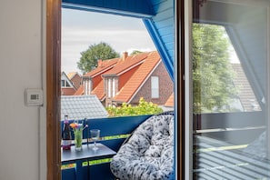 A room with a view of neighboring houses, a table with a bottle and glass, and a floral-patterned chair. - Holiday Home 'Lotte' with Sea View, Private Terrace and Wi-Fi (Wittmund)