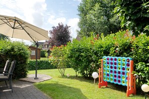A garden with a lawn, a wooden bench, a metal umbrella, and a colorful play structure. - Holiday Home 'Lotte' with Sea View, Private Terrace and Wi-Fi (Wittmund)