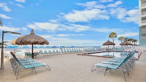 Un área junto a la piscina con sillones de descanso, sombrillas y vista al océano.