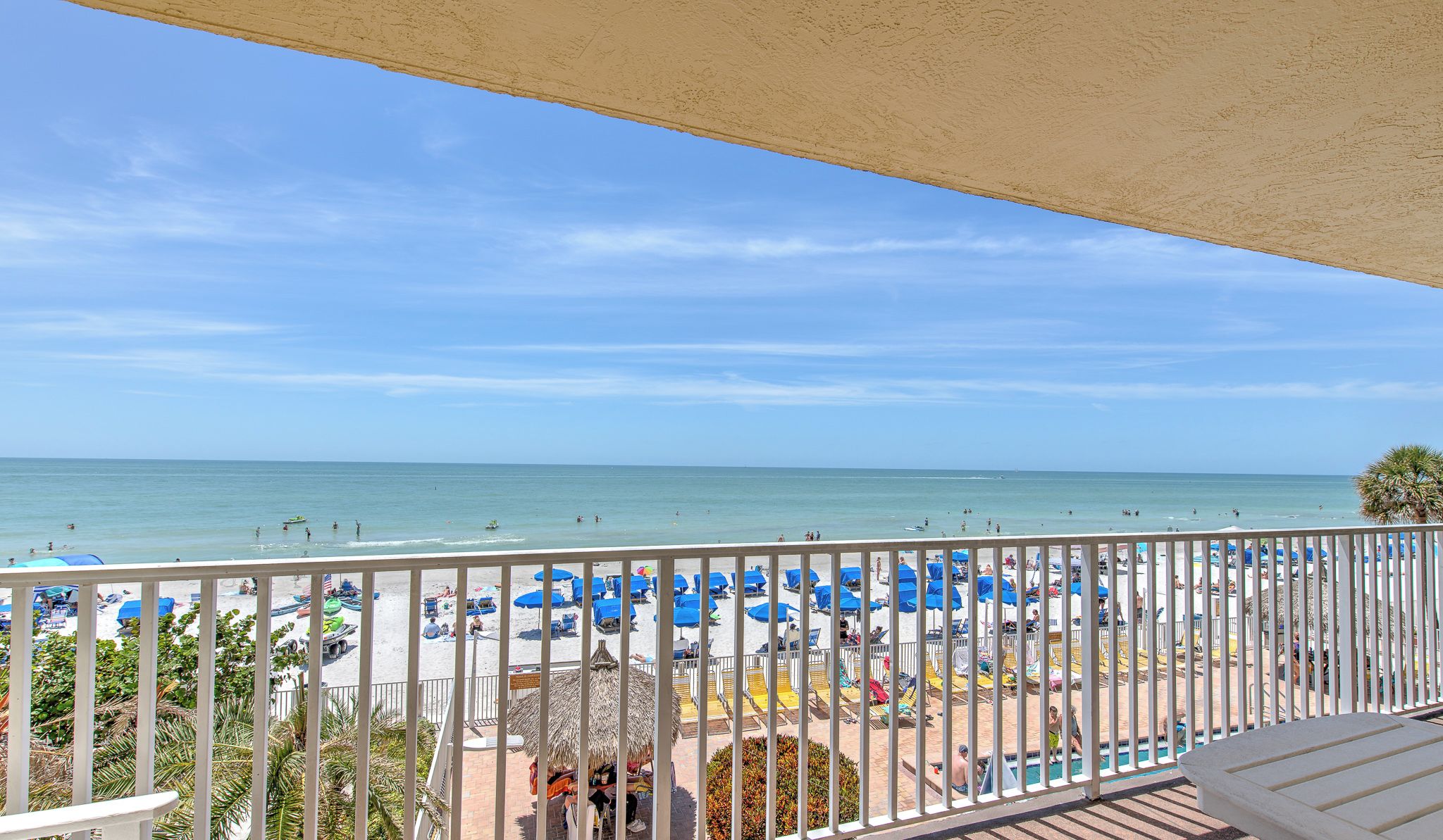 A balcony with a view of a beach, featuring a pool area, umbrellas, and lounge chairs.