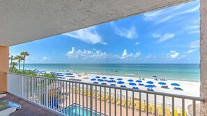A balcony with a view of a beach, sun loungers, and a pool.