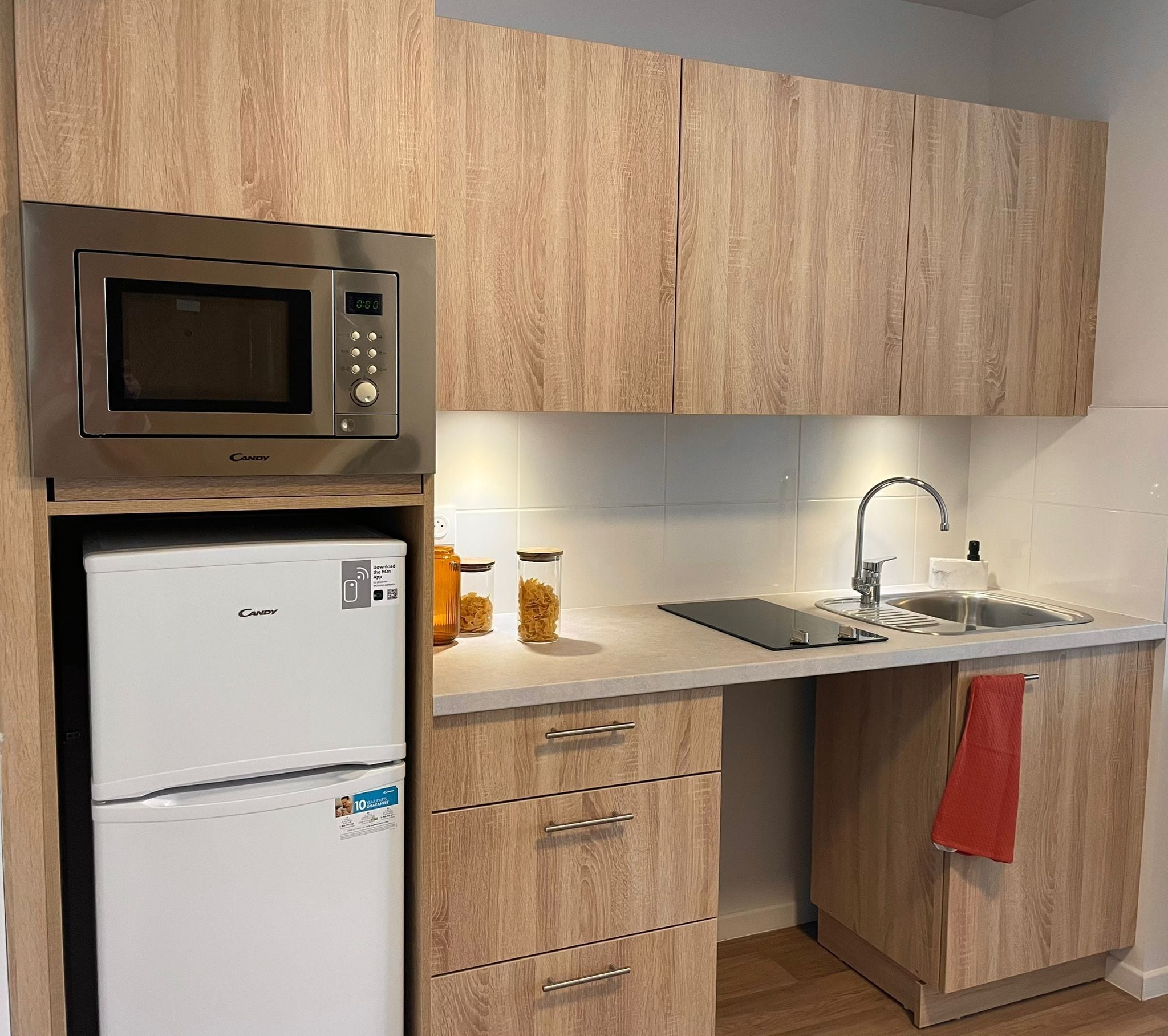 A compact kitchen with a microwave, refrigerator, sink, and wooden cabinets.