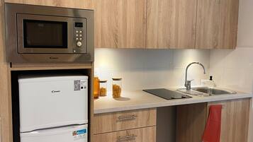 A compact kitchen with a microwave, refrigerator, sink, and wooden cabinets.