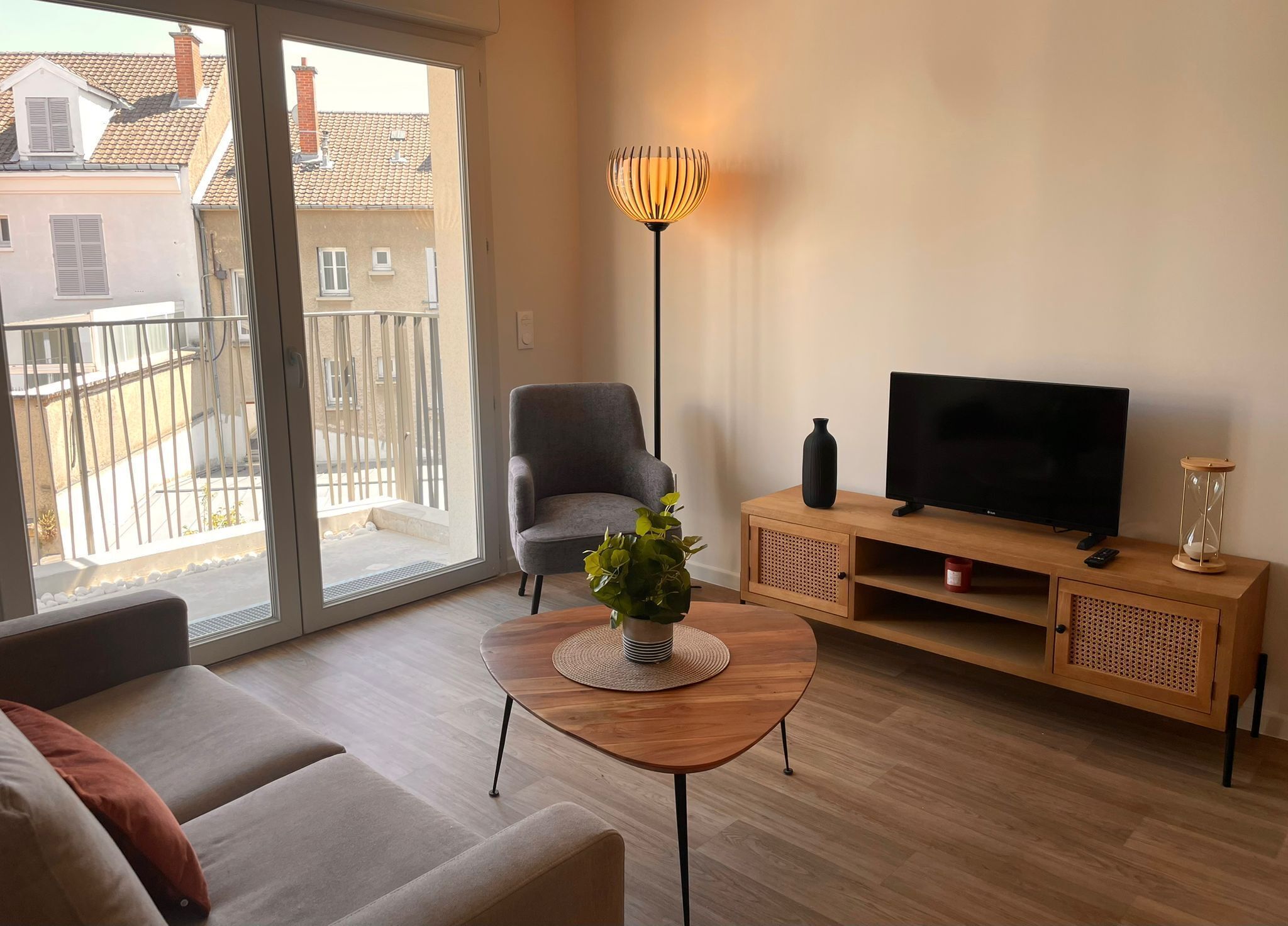 Una sala moderna con un sofá, una mesa de centro con una planta, un televisor sobre un mueble de madera y una lámpara de pie.