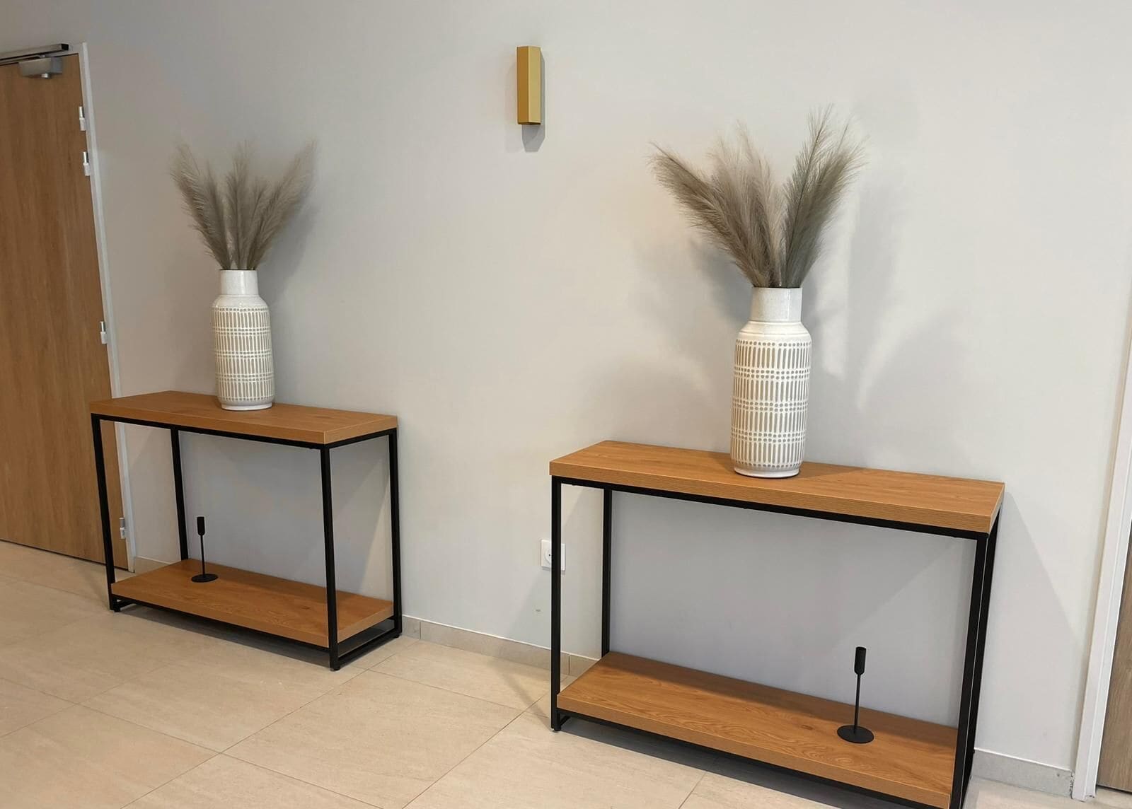 Two white vases with pampas grass on a wooden console table against a plain wall.