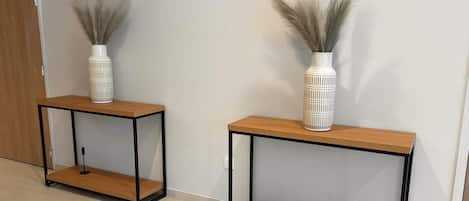 Two white vases with pampas grass on a wooden console table against a plain wall.