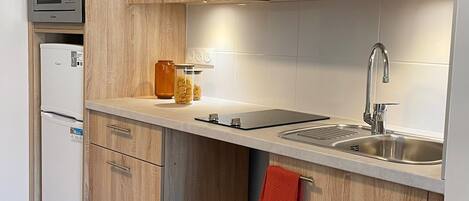 A modern kitchen with wooden cabinets, a built-in microwave, a refrigerator, a sink, and a countertop with a red towel.