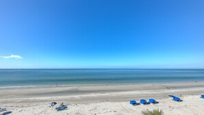 Una playa con cielos despejados, agua tranquila y varias sombrillas azules.