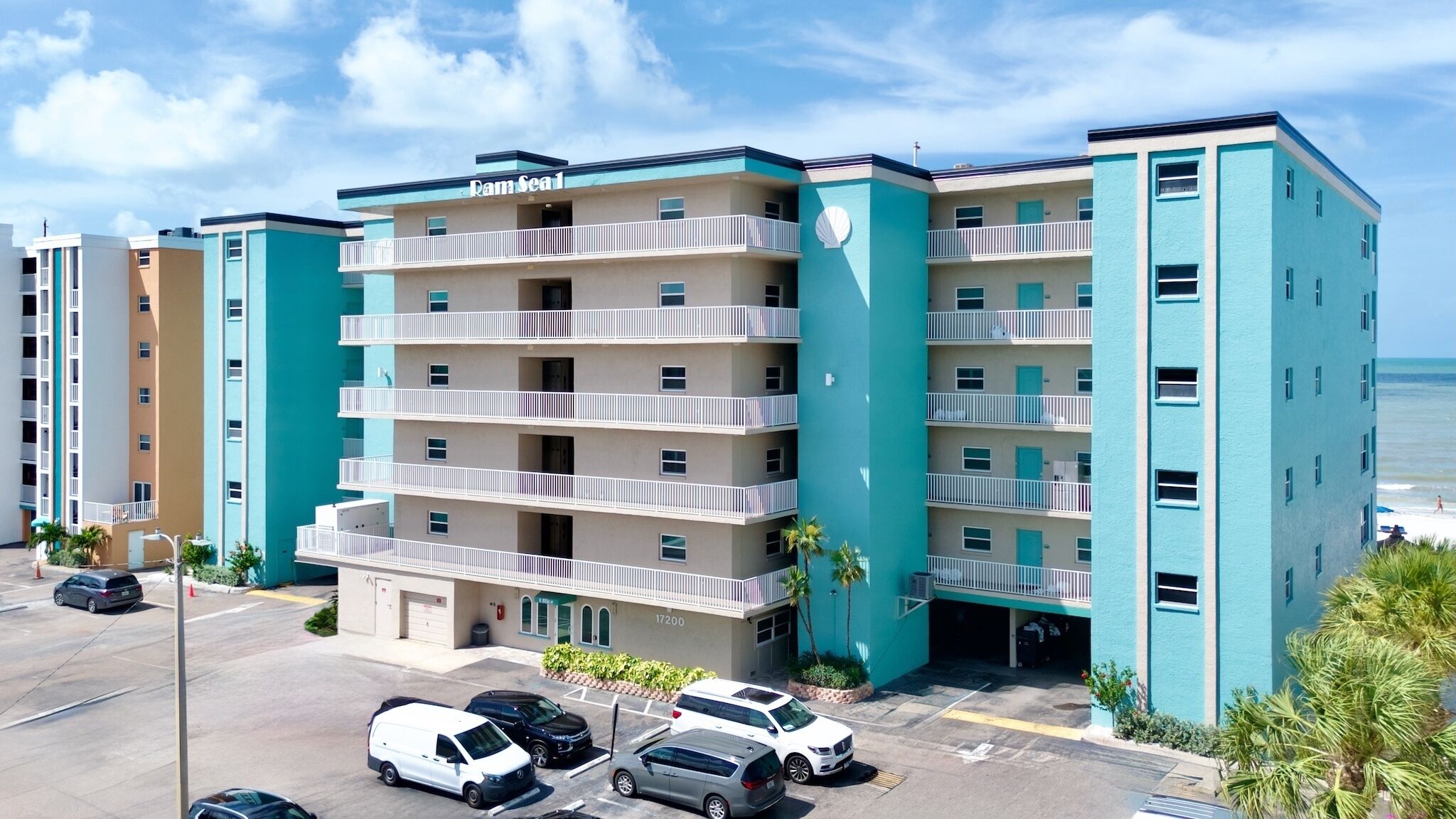 A multi-story hotel with balconies, a parking lot, and a view of the ocean.