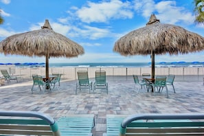 Eine Terrasse am Strand mit StrohdĂ€chern, grĂŒnen StĂŒhlen und Blick aufs Meer.