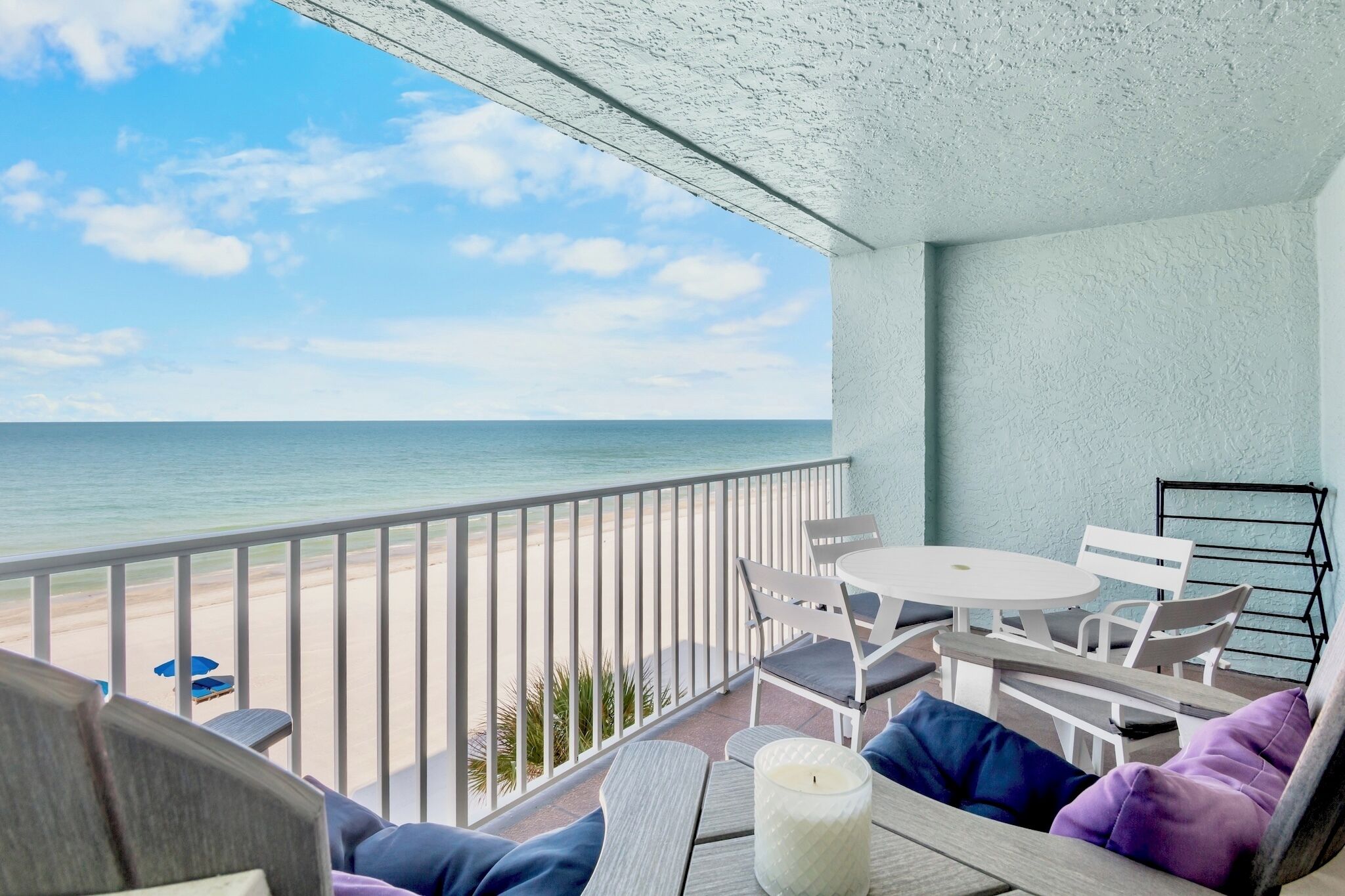 Ein Balkon mit Blick auf Strand und Meer, ausgestattet mit Tisch, Stühlen und Kissen.