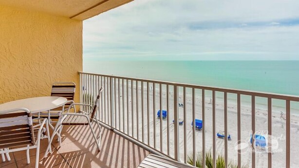 Un balcón con vistas a la playa, una mesa y sillas.