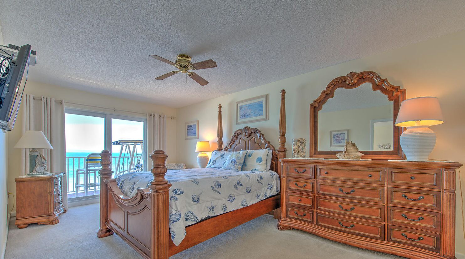 Quarto com cama, penteadeira, ventilador de teto e varanda com cadeiras.