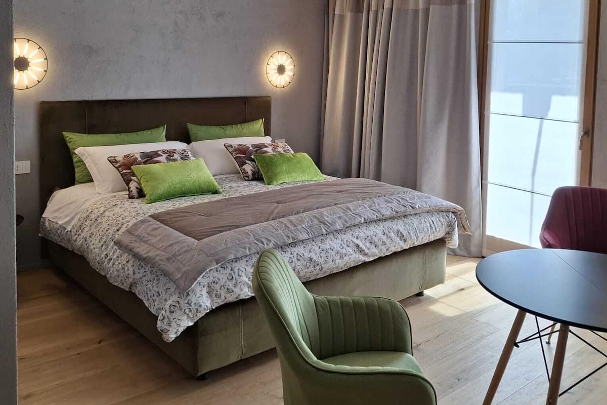 A modern bedroom with a large bed, two wall sconces, a dining table, and a view of the outdoors.