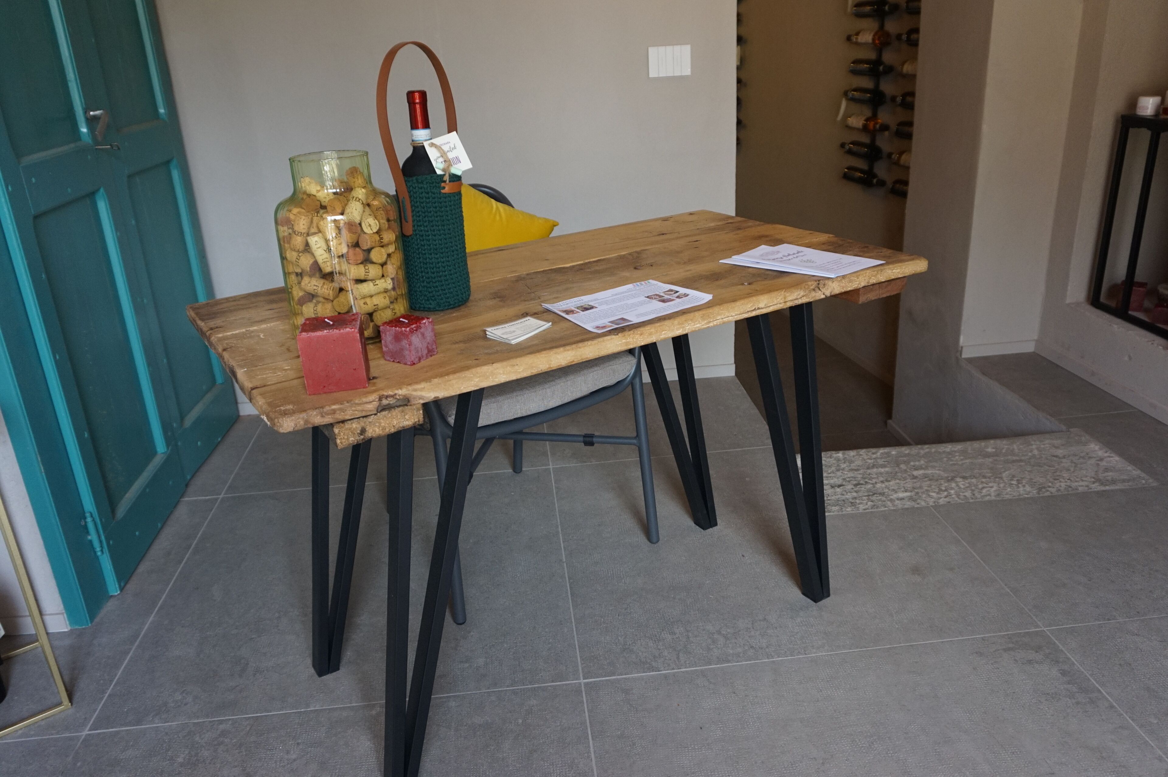 A wooden table with a bottle of wine, a green bag, and some papers.