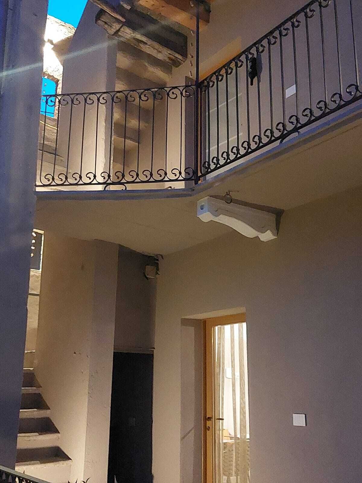 Un edificio de varios niveles con balcón, escaleras y una puerta que da a un espacio interior.