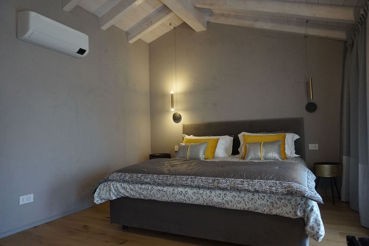 A bedroom with a large bed, a bedside table, a wall-mounted air conditioner, and a hanging light fixture.