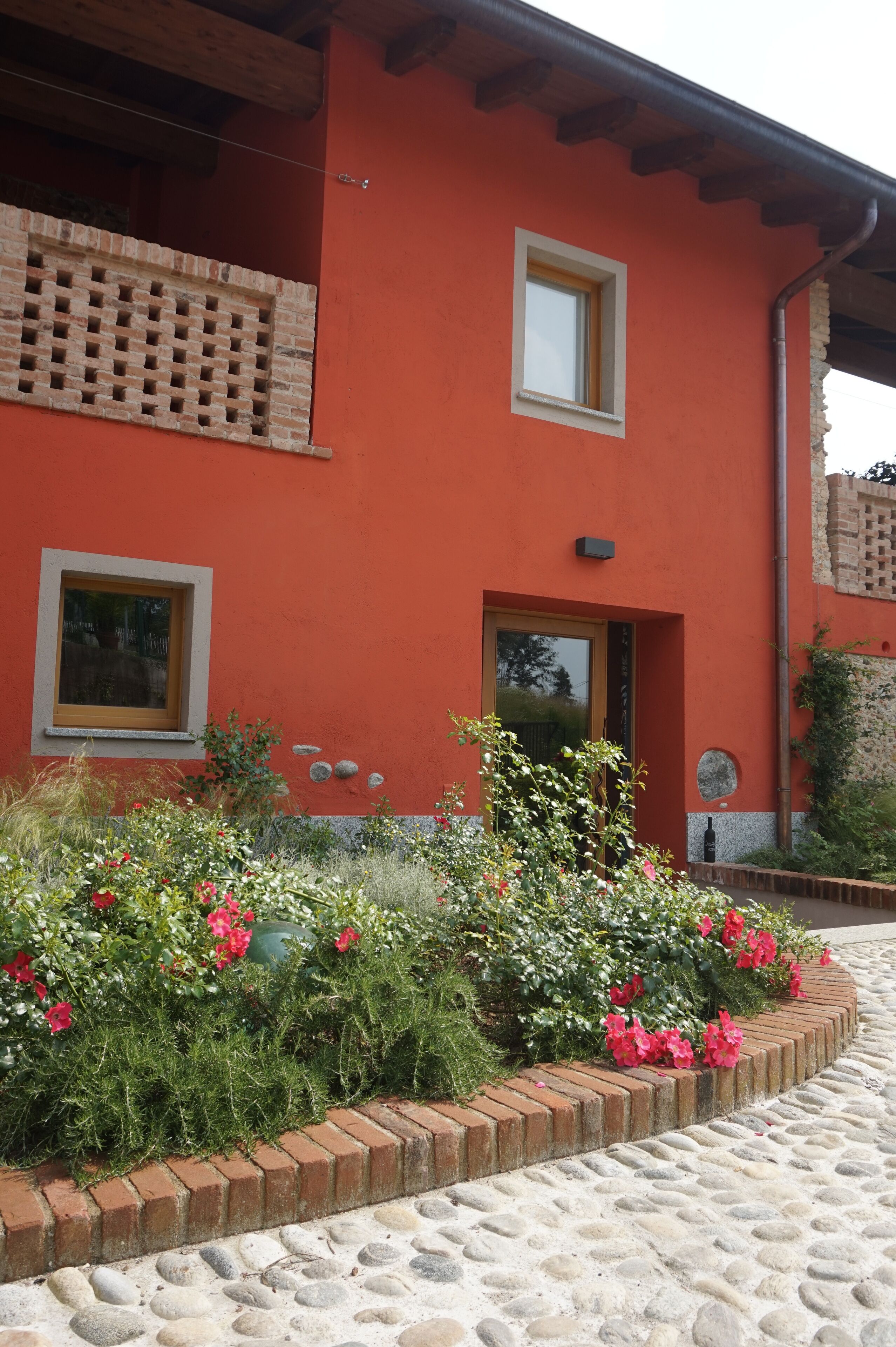 Un edificio rojo con balcón, ventana y puerta. Hay un jardín con flores y un sendero de piedra.