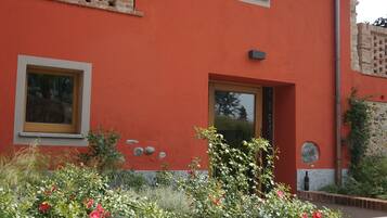 Un edificio rojo con balcón, ventana y puerta. Hay un jardín con flores y un sendero de piedra.