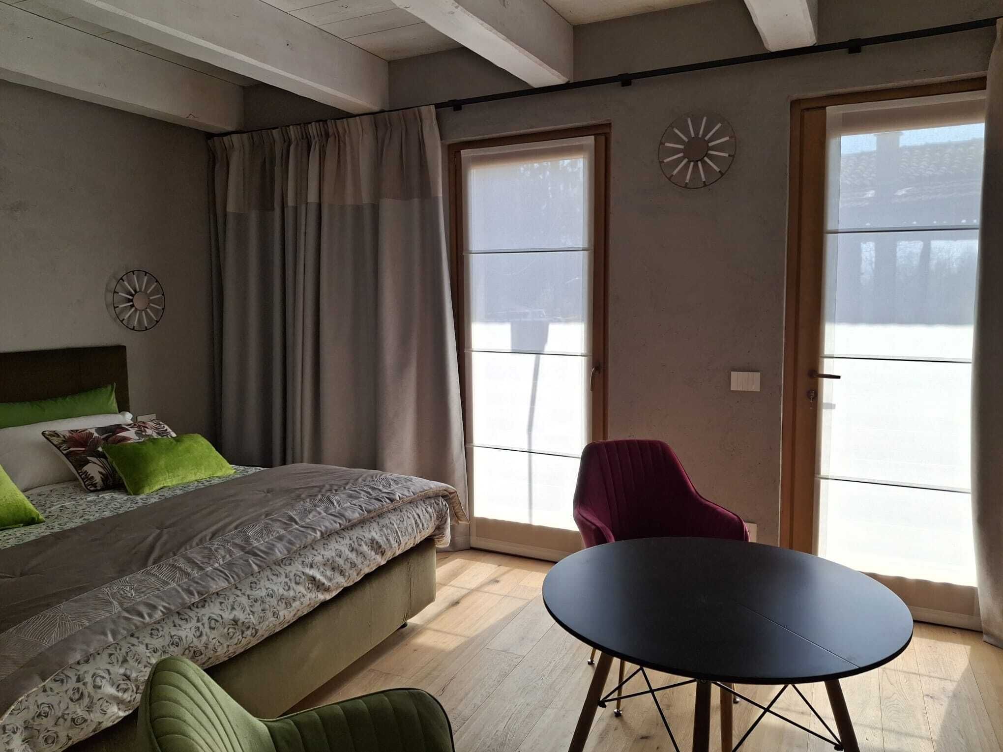 Un dormitorio con una cama, una silla verde, una mesa negra y una ventana con cortinas.