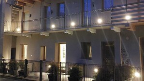 Un edificio de varios pisos con balcones, entrada protegida por un portón y plantas en macetas.